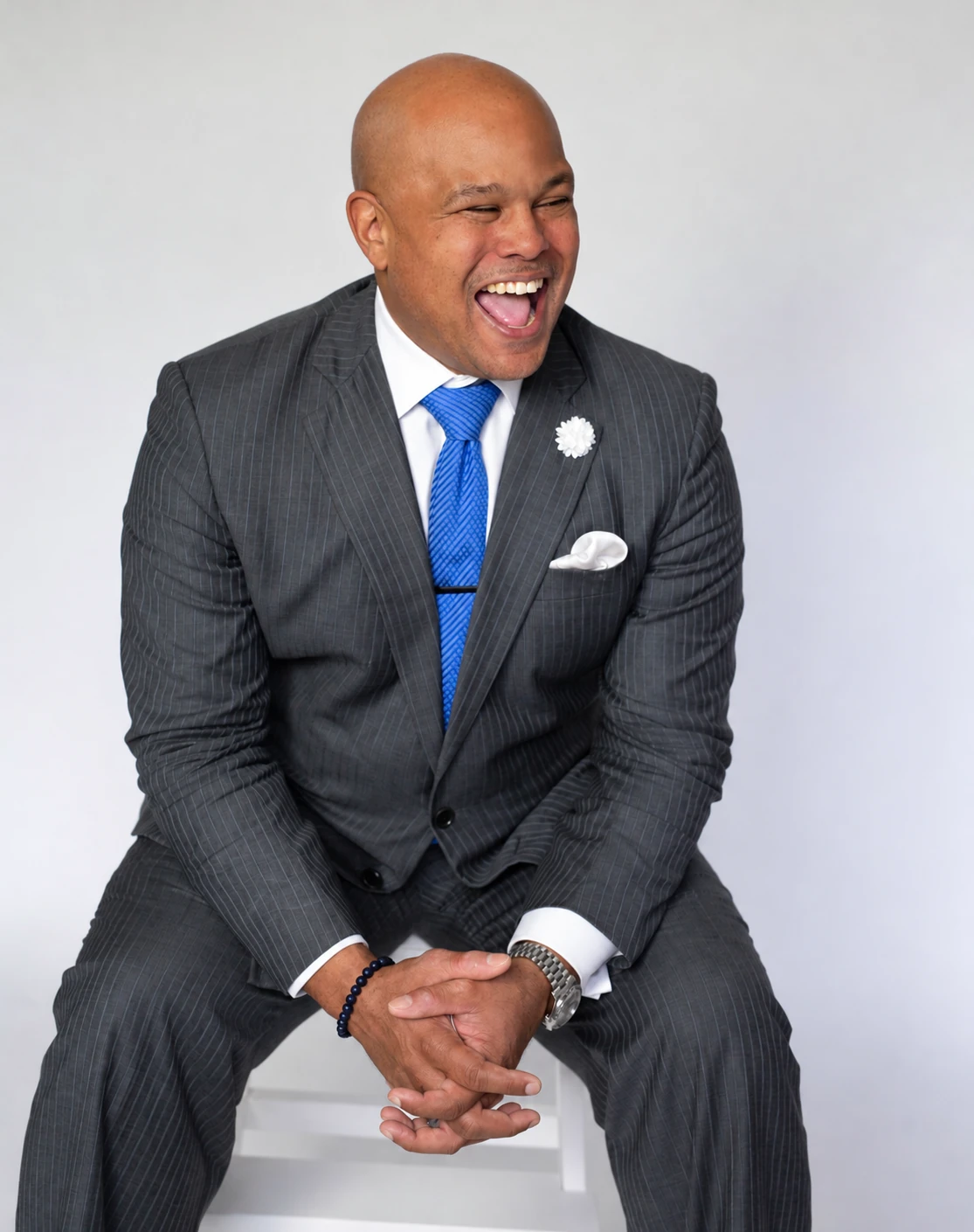 David Wilson laughing, seated in a pinstripe suit and blue tie